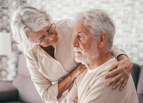 a senior woman wraps her arm around her husband's shoulders